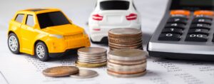Mini toy cars next to a stack of coins and a calculator.