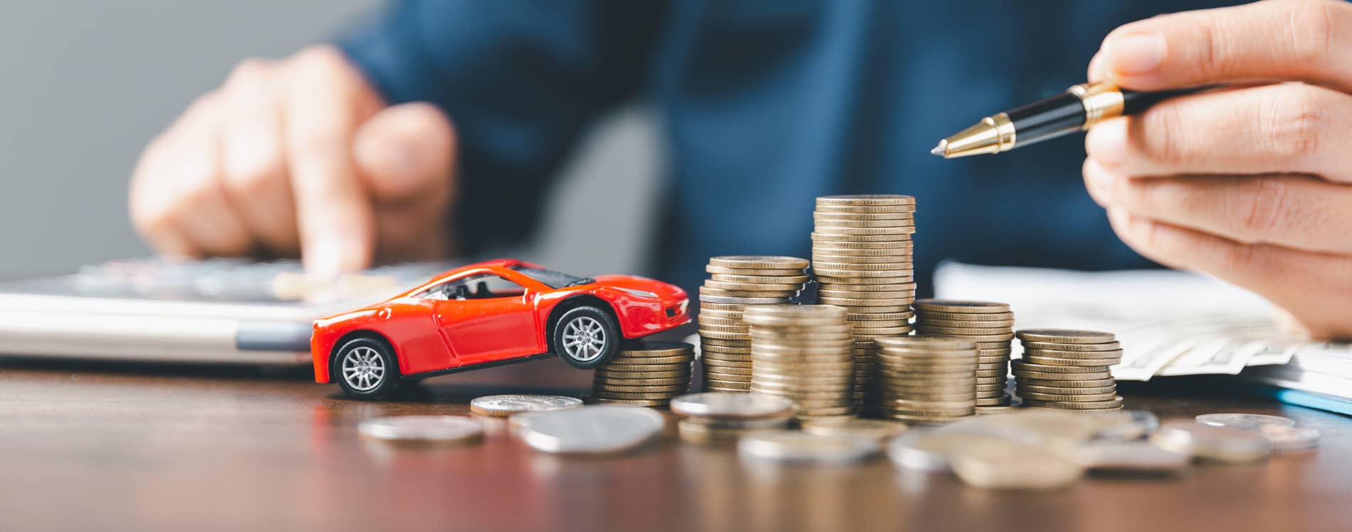Person calculating finances with a calculator, stack of cars and toy car resting on a table.