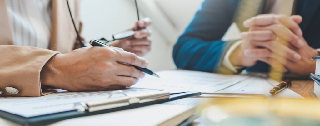 A lawyer speaking to a partner while holding a pen next to paperwork.